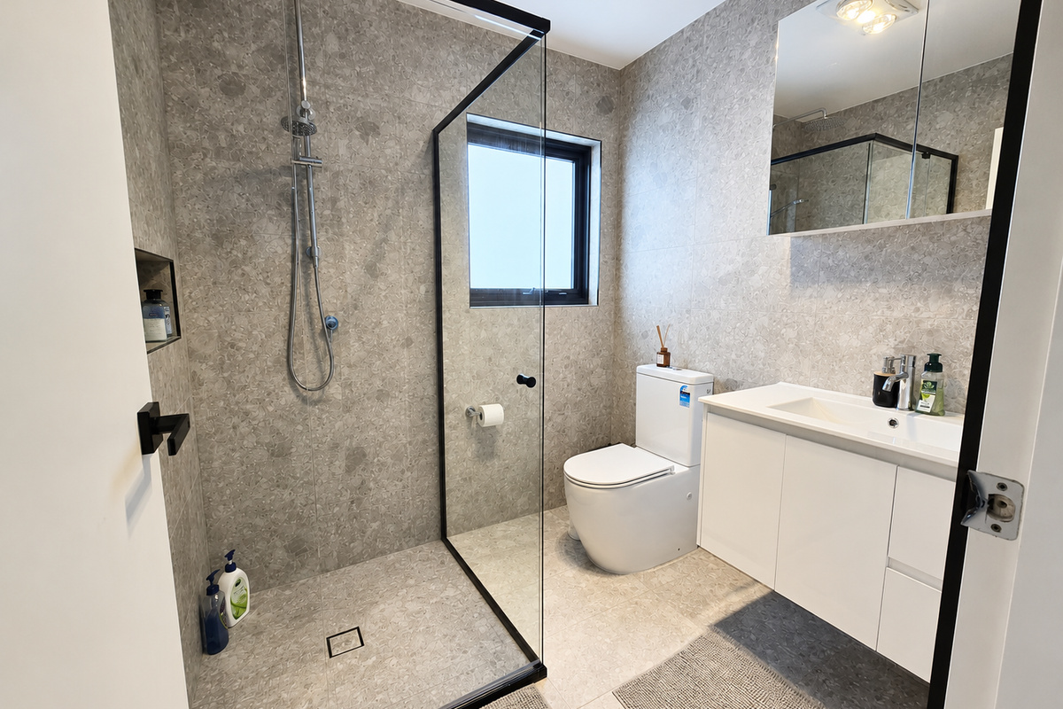 Matilda’s Urban Escape includes a full bathroom with grey floor-to-ceiling tiles, glass shower screen, vanity, mirror cabinet and toilet.
