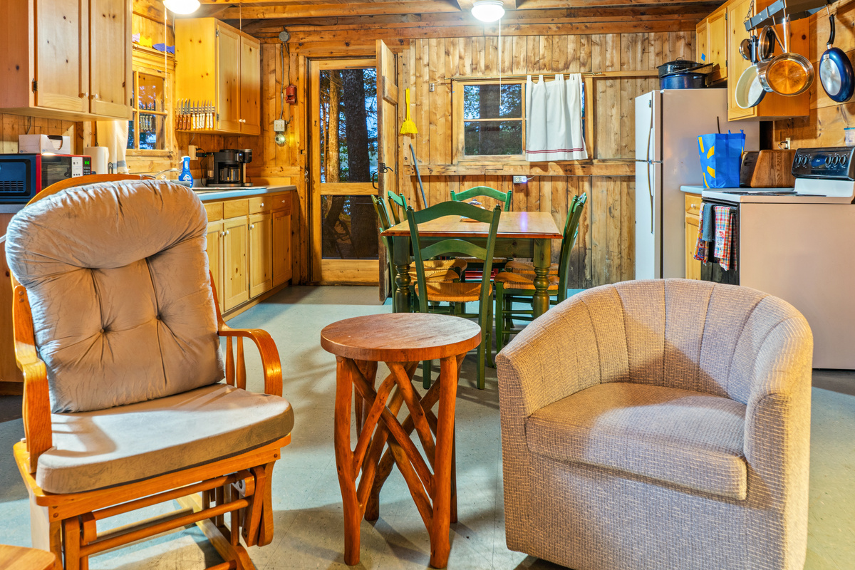Comfortable living room seating at Loonrise Point! Glider and swivel armchair showcase the open-concept flow into the dining area and fully equipped kitchen beyond. Bright, connected interior layout on Beech Hill Pond in Otis, ME.