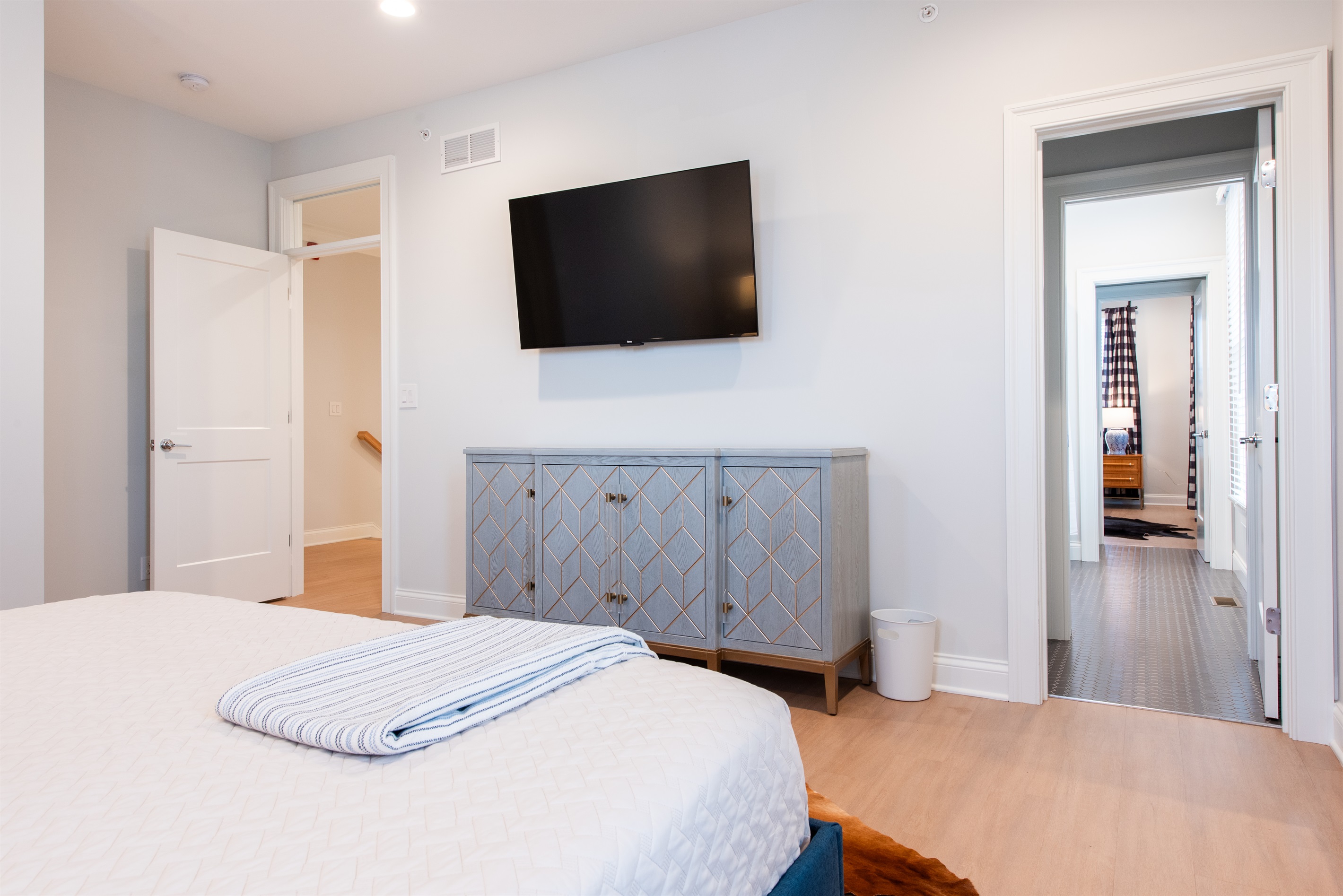 Enjoy your stay in this spacious, stylish bedroom featuring a king bed and a large, wall-mounted flat-screen TV. The elegant decor and hardwood floors create a warm and inviting atmosphere, perfect for relaxation on the Bourbon Trail.