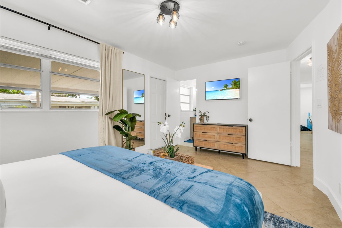 A bright and inviting primary suite featuring a hotel-quality king bed, dramatic pendant lighting, a sleek ensuite shower bath, and a Smart Fire streaming TV—your perfect private sanctuary.