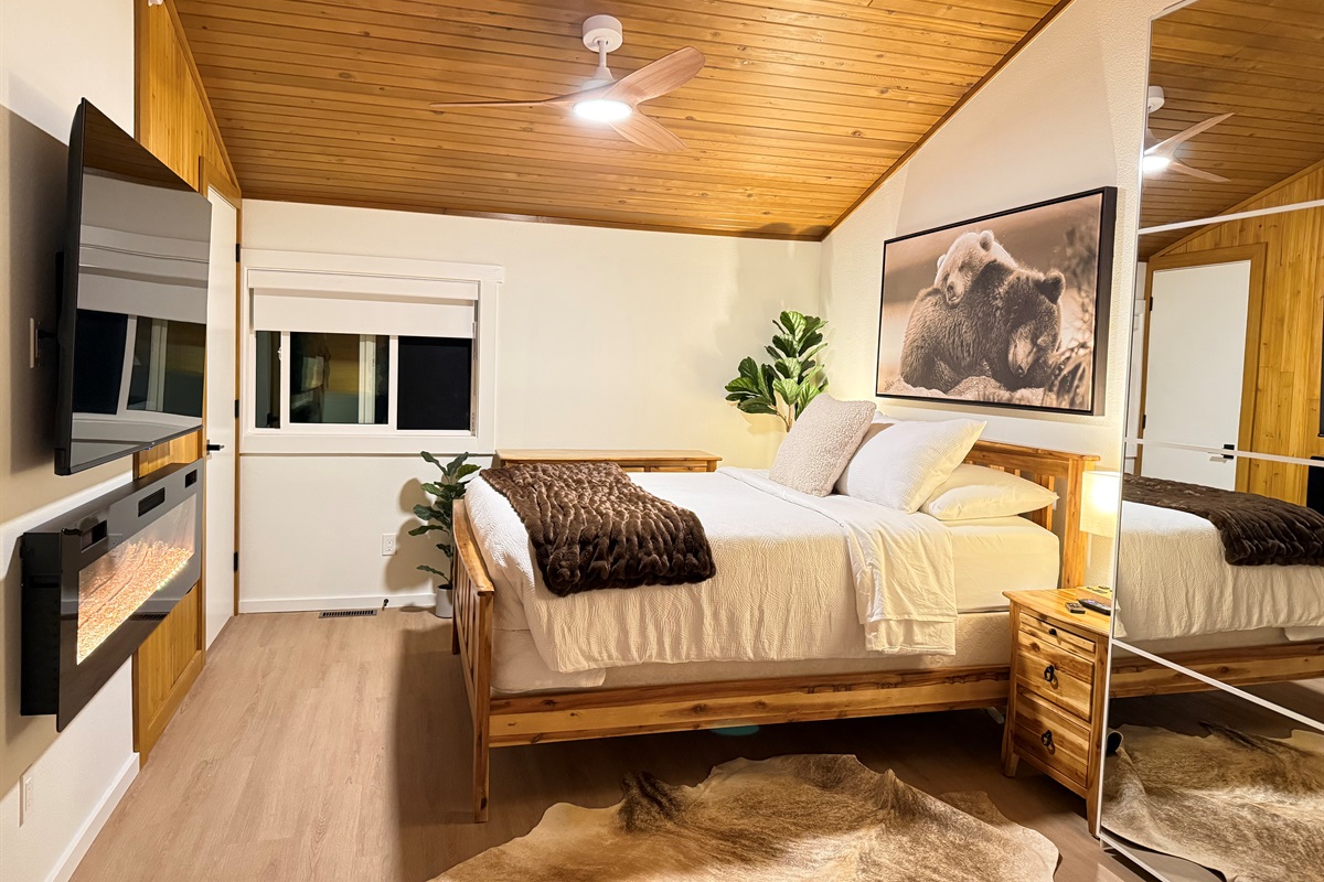 A romantic loft bedroom suite with alpine decor, a 65" TV, electric fireplace, closet and dresser storage. 