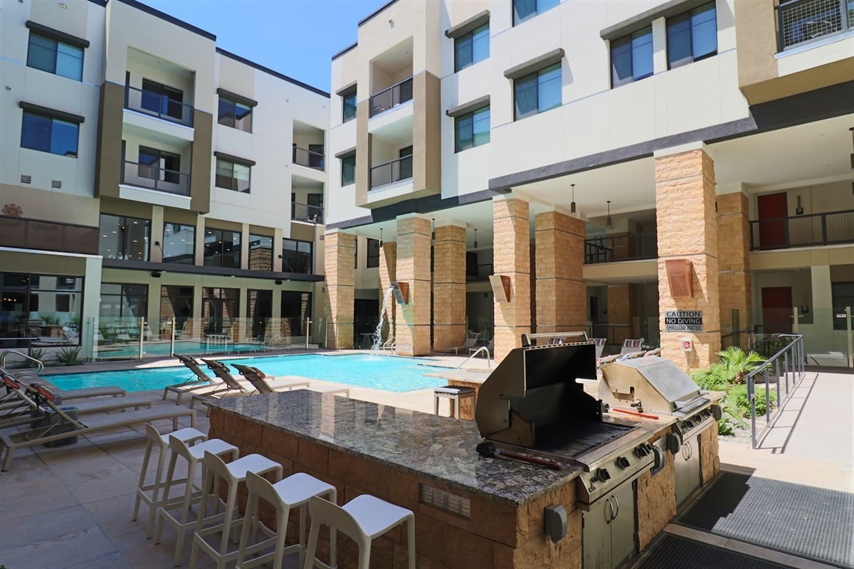 - Enjoy outdoor cooking with a full BBQ grill setup beside the bright pool area   - Bar seating and lounge chairs make it ideal for gatherings and relaxation   - Perfect for summer evenings filled with good food and friendly conversations
