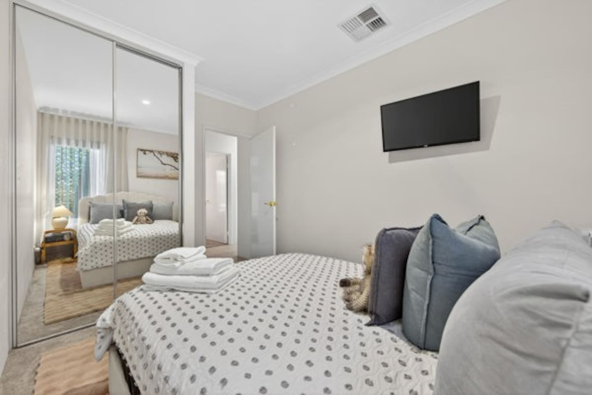 Relaxing bedroom with a wall-mounted TV, mirrored built-in robe, ducted air conditioning and fresh towels laid out on the bed.