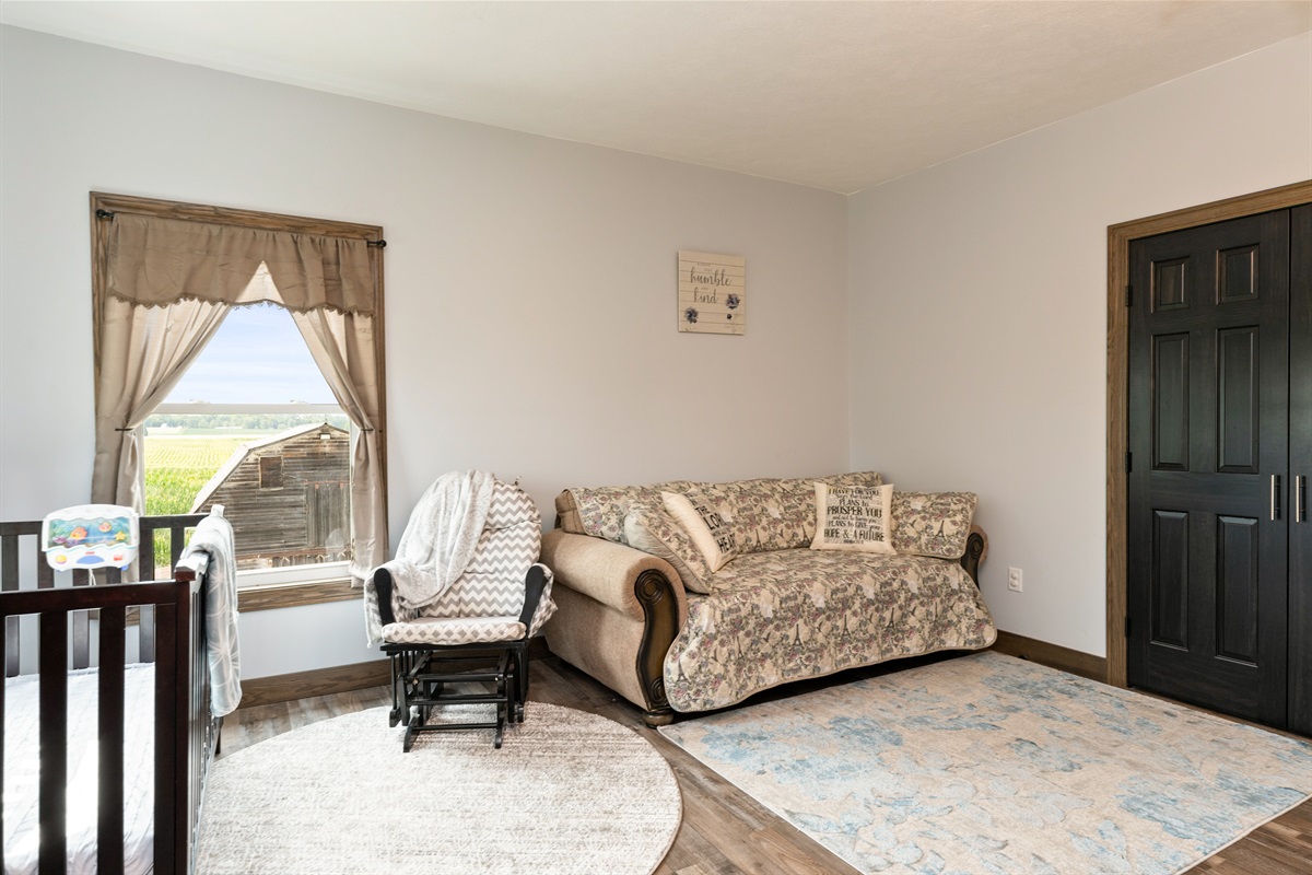A bright and spacious master bedroom featuring a cozy queen bed, Queen fold out sofa and crib with elegant wood furniture, and stunning countryside views through large windows. Perfect blend of comfort and charm for a restful stay. Bedroom #1
