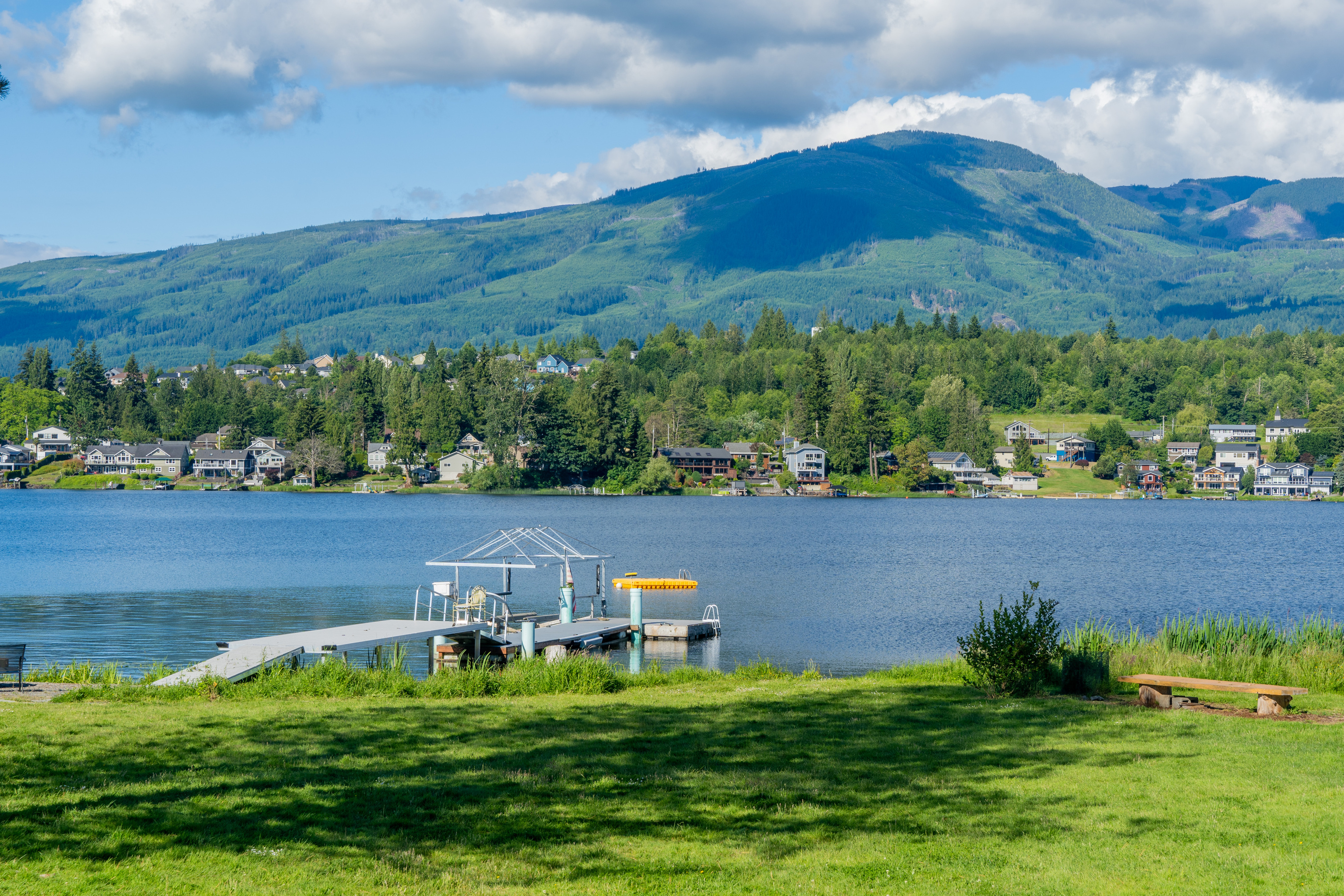 Looking out across the lake, the dock rests to the right along the shoreline. Calm water reflects the sky and surroundings, creating a peaceful, inviting scene of the lakeside setting.