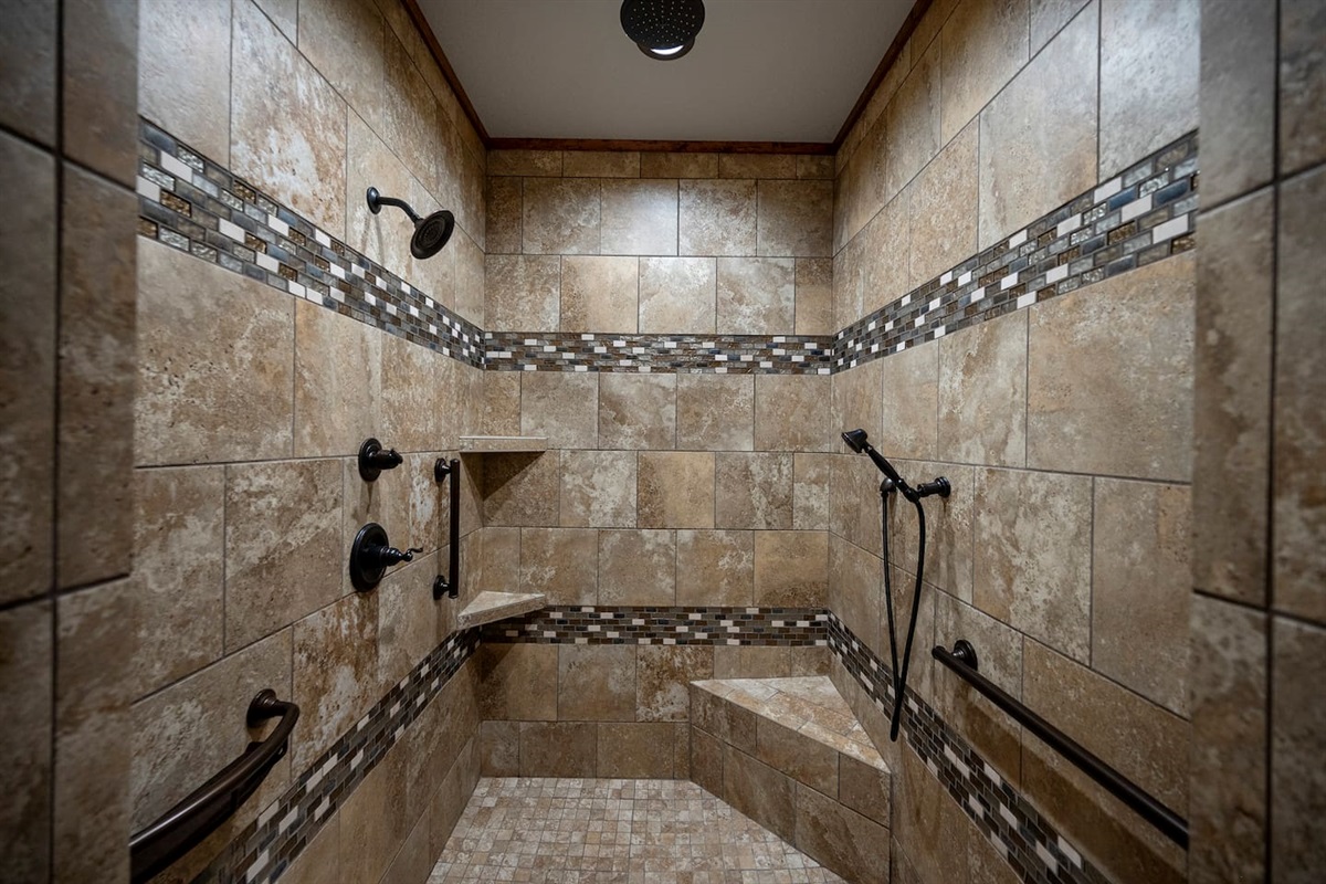 Primary bathroom has a walk in open shower with handrails and a rain shower head