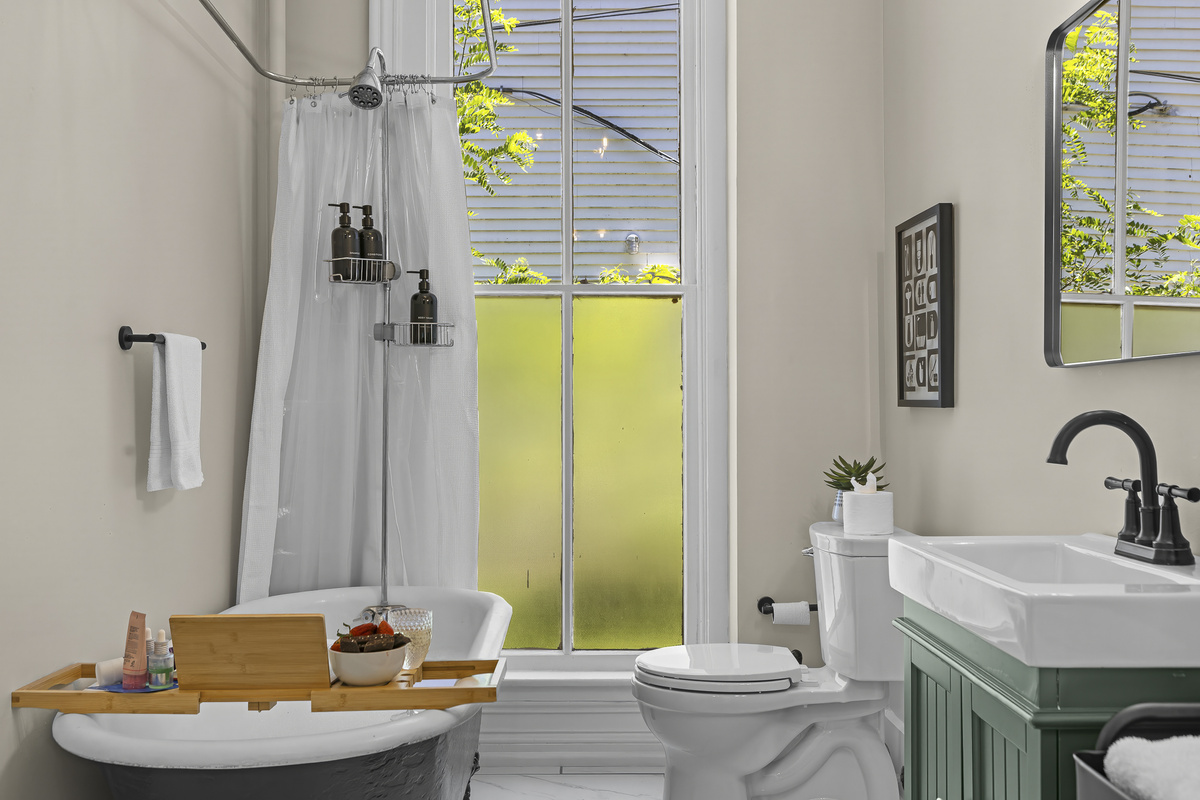 The clawfoot soaking tub is styled for a proper soak. Bamboo bath caddy, botanicals, and a tree-canopy window.