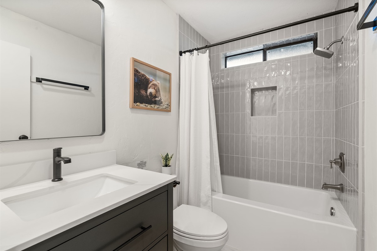 Bright and stylish bathroom with a stone countertop, single vanity, and tiled tub surround—perfect for a relaxing soak