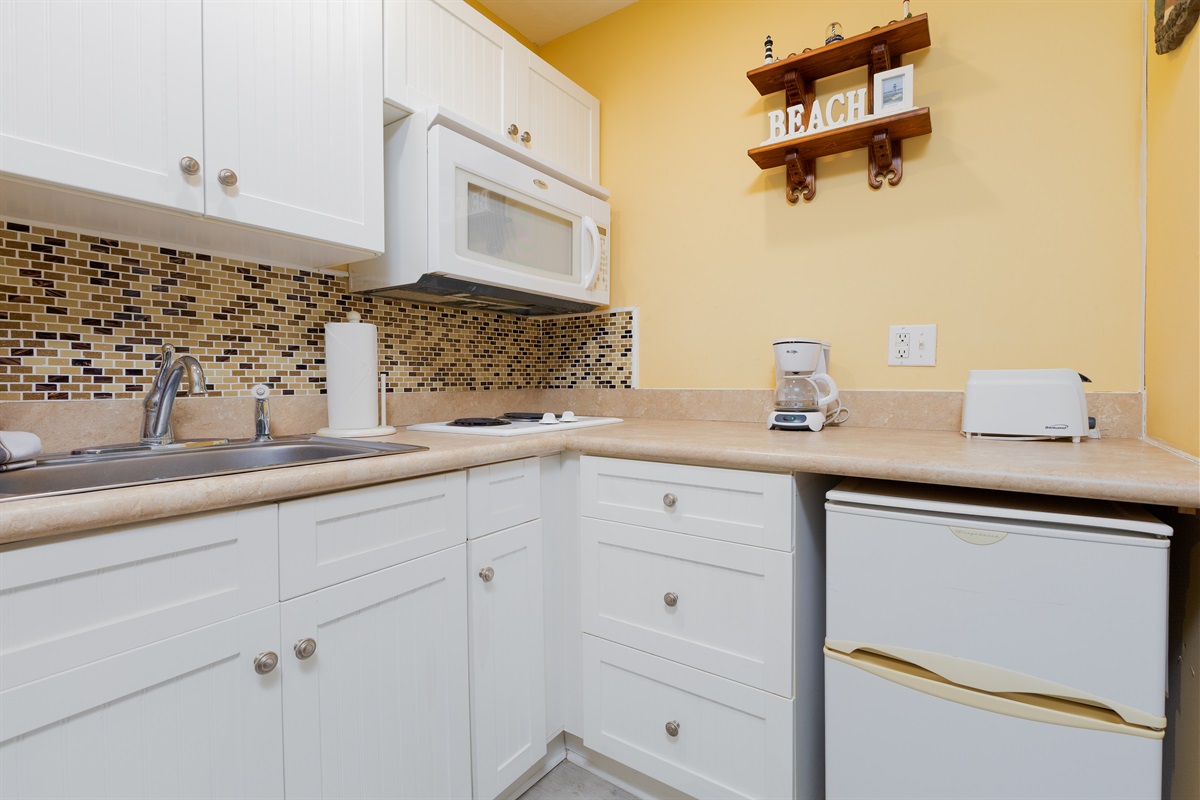 Compact kitchenette equipped with a mini fridge, microwave, coffee maker, toaster, and essentials for easy meals during your beach stay