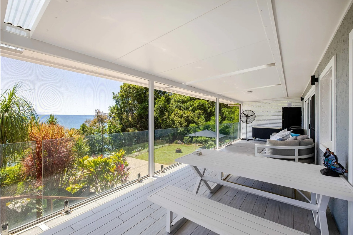 This sheltered outdoor area includes a picnic-style dining table, lounge seating and glass balustrade for easy deck living.