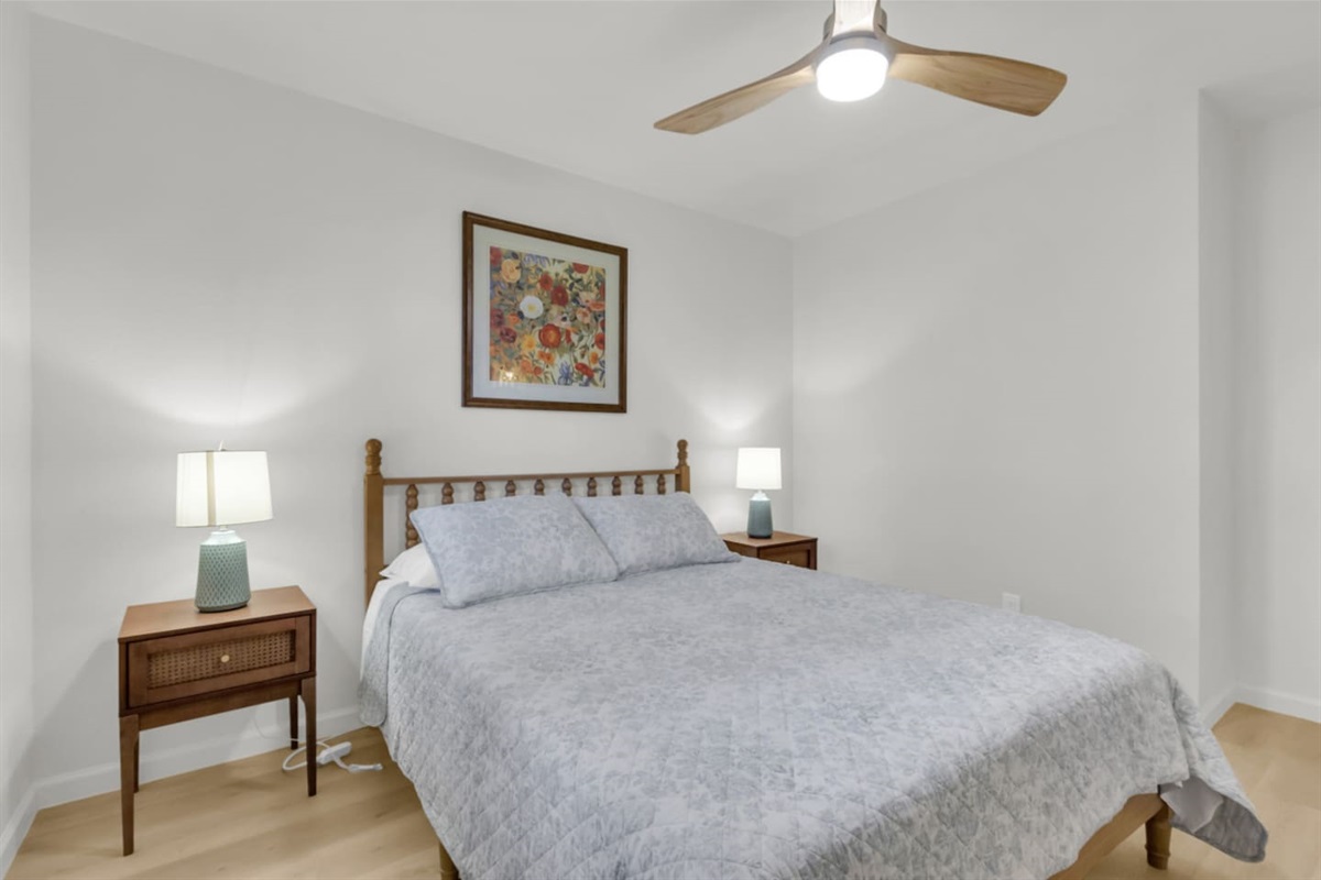 Bright guest room featuring a queen bed, soft bed linens, and a modern ceiling fan for added comfort. A calm, minimalist space perfect for restful nights.