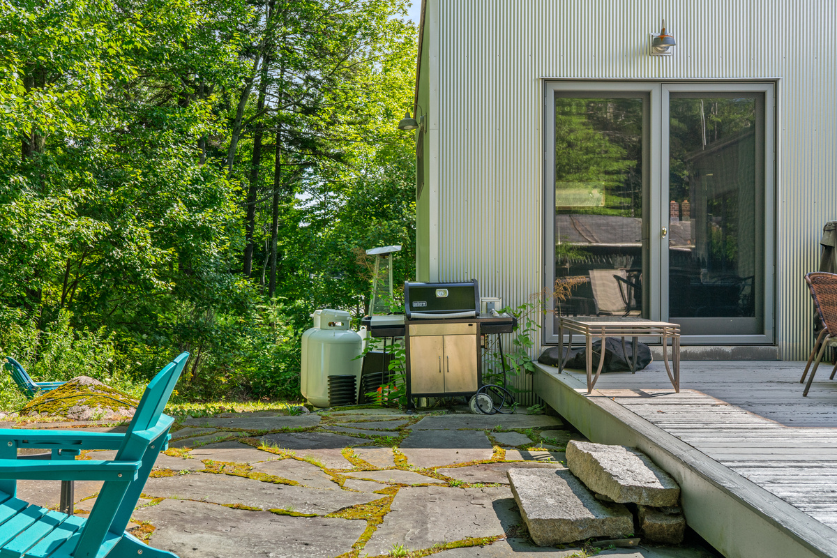 Outdoor cooking and seamless flow at "The Crag." Fire up the Weber gas grill on the flagstone patio, then step right onto the 33-foot deck or into the primary suite—all framed by the direct woods of Acadia National Park.