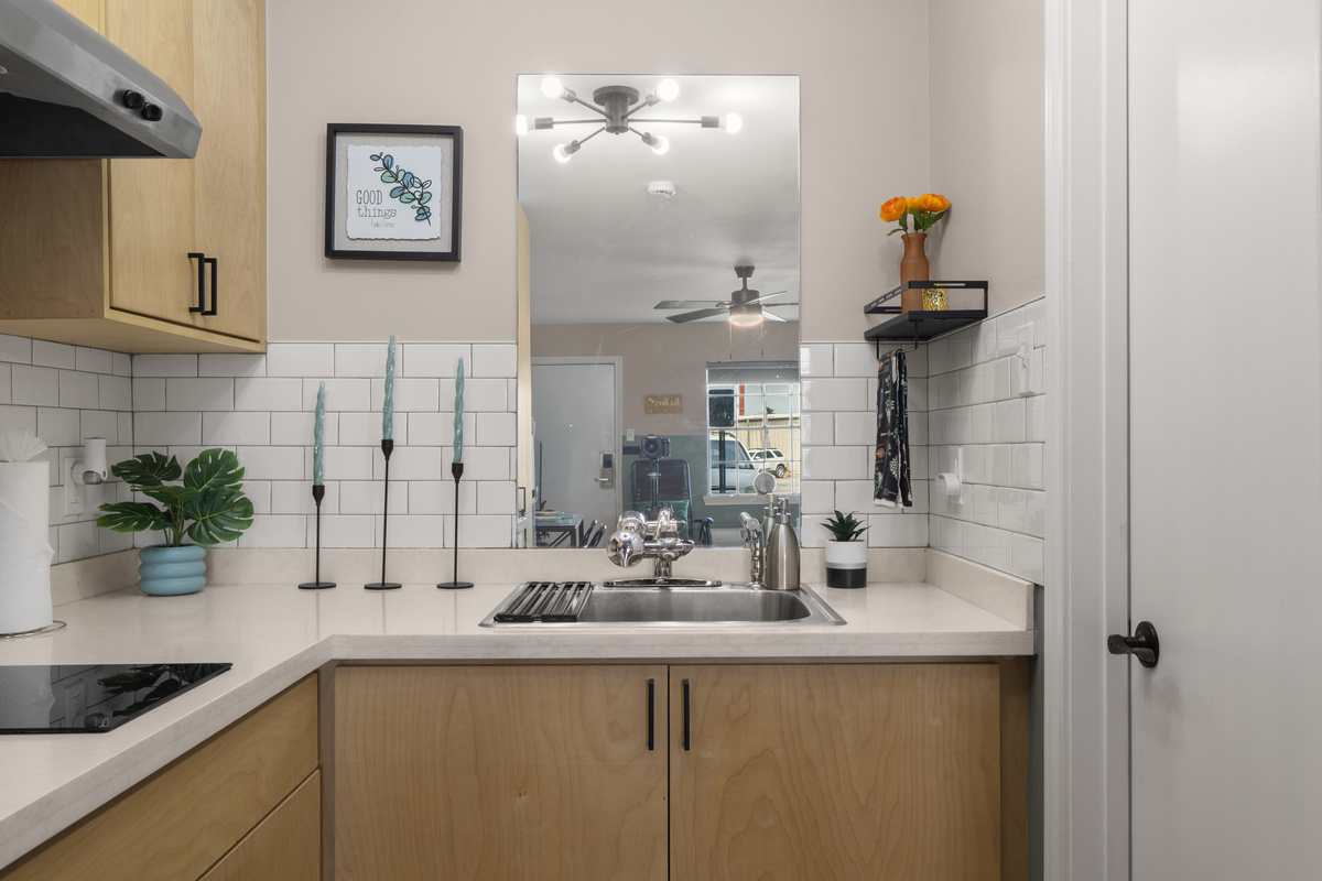 Kitchenette sink area with cabinet storage, counter space, and a mirror that keeps the room feeling open.
