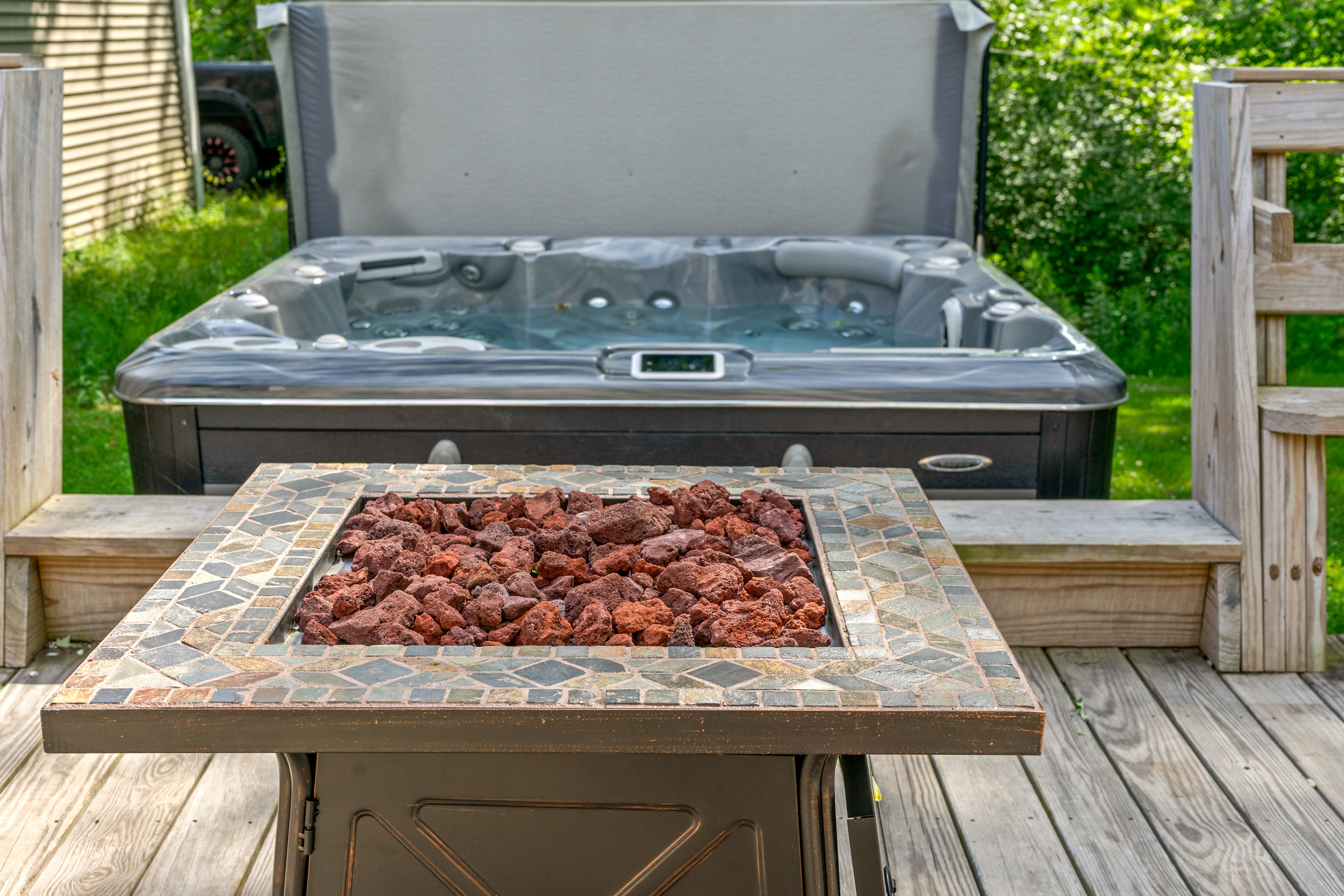 Soak in the private 6-person hot tub while enjoying the warmth of the adjacent propane fire table. This intentional deck layout positions both premium amenities side-by-side, creating a seamless outdoor relaxation area on the wooden deck.