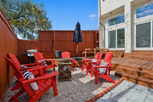 Fully fenced private backyard featuring a spacious deck and gravel lounge area with Adirondack seating around a fire feature. Enjoy outdoor dining, string lights for evening ambiance, and plenty of space to relax or gather with family and friends.