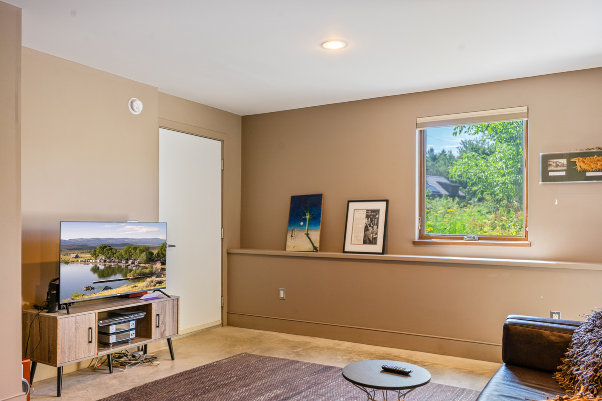The home’s primary media room located on the lower level, featuring a smart Roku TV and cozy lounge area. This dedicated social space offers a quiet retreat for movie nights, positioned conveniently between the guest bedroom and the private garage.