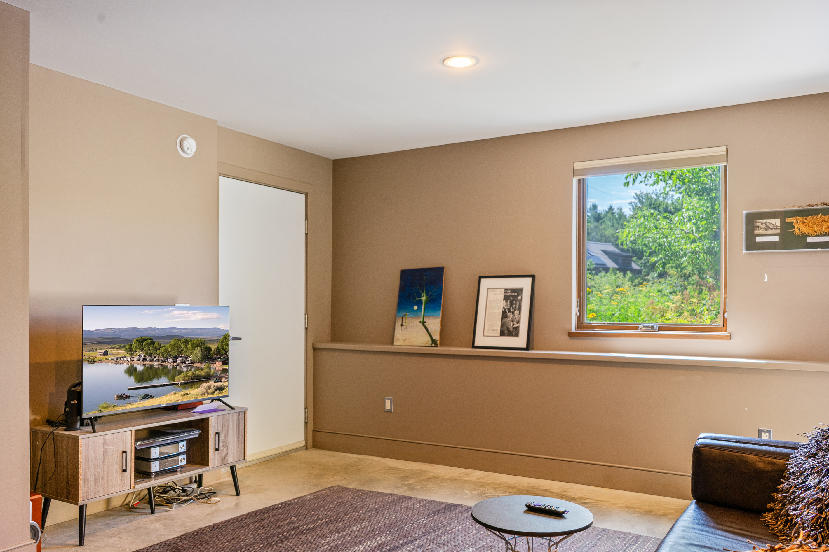 The home’s primary media room located on the lower level, featuring a smart Roku TV and cozy lounge area. This dedicated social space offers a quiet retreat for movie nights, positioned conveniently between the guest bedroom and the private garage.