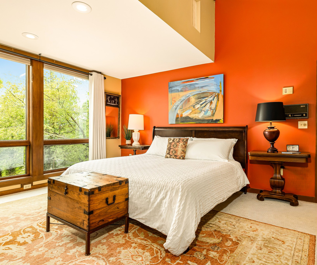 Main-floor primary suite featuring a premium Helix King bed, high ceilings, and large windows overlook the private, treed property. Decorated with vintage furniture and an antique area rug, just steps from the full en-suite bath.
