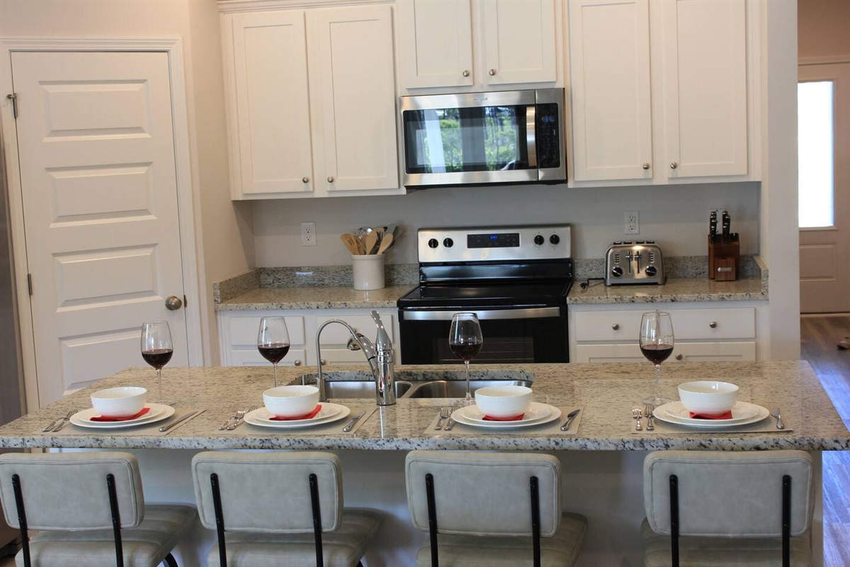 Bright full kitchen with counter seating for 4, a stove, microwave, sink, and 2-door fridge.