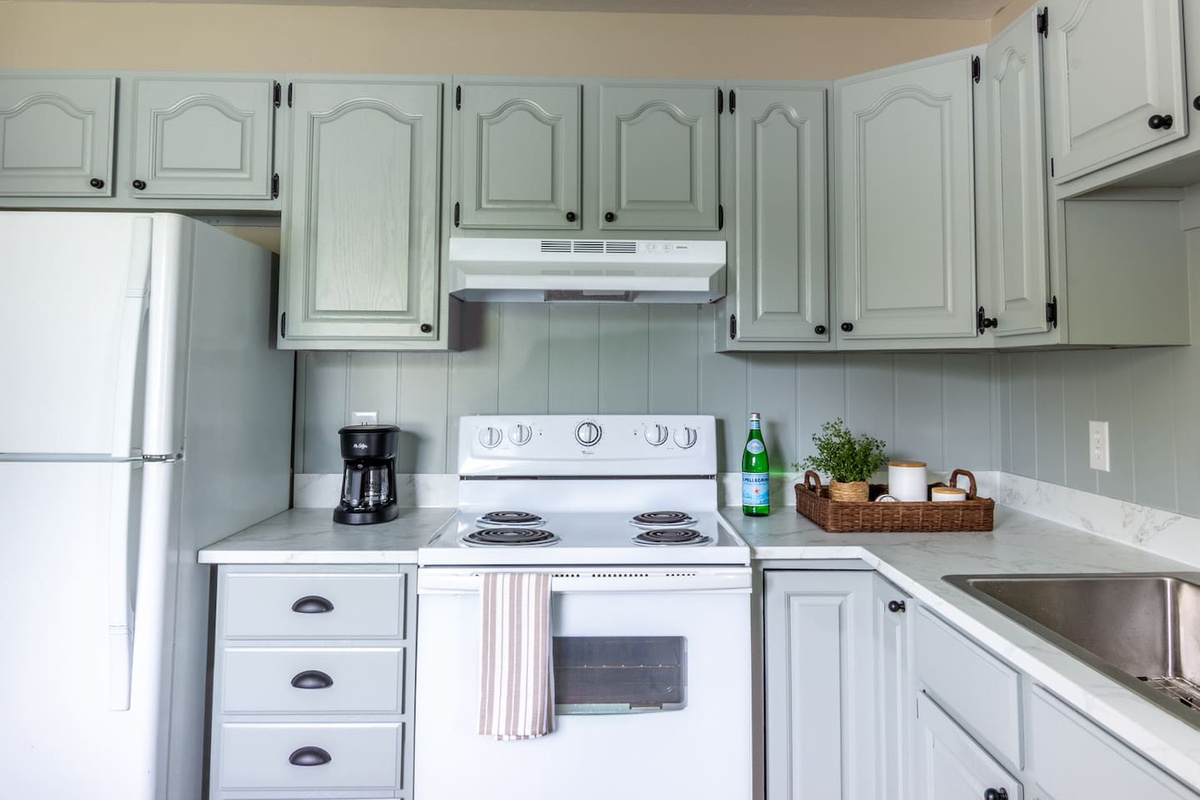 Classic white appliances and soft green cabinetry make the cook space feel bright and welcoming.