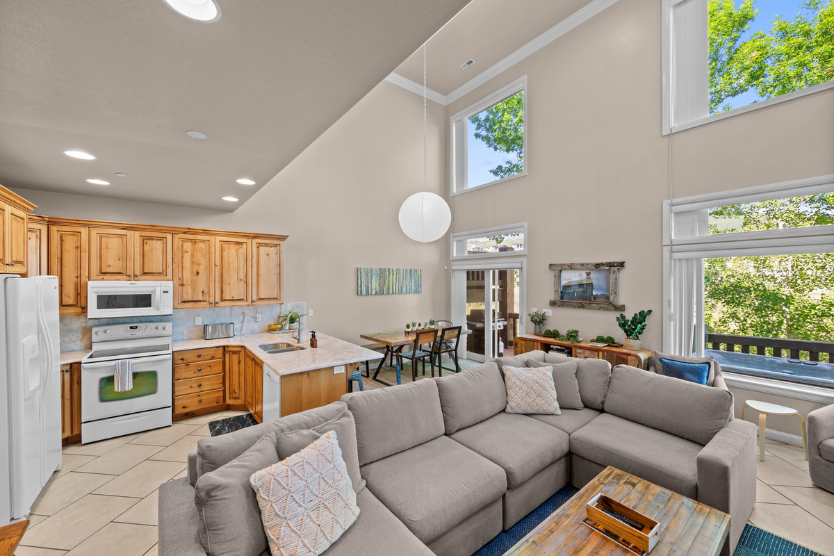 Bright and airy open-concept living space featuring vaulted ceilings, a fully equipped kitchen, cozy sectional seating, and large windows showcasing beautiful Pineview Reservoir views.