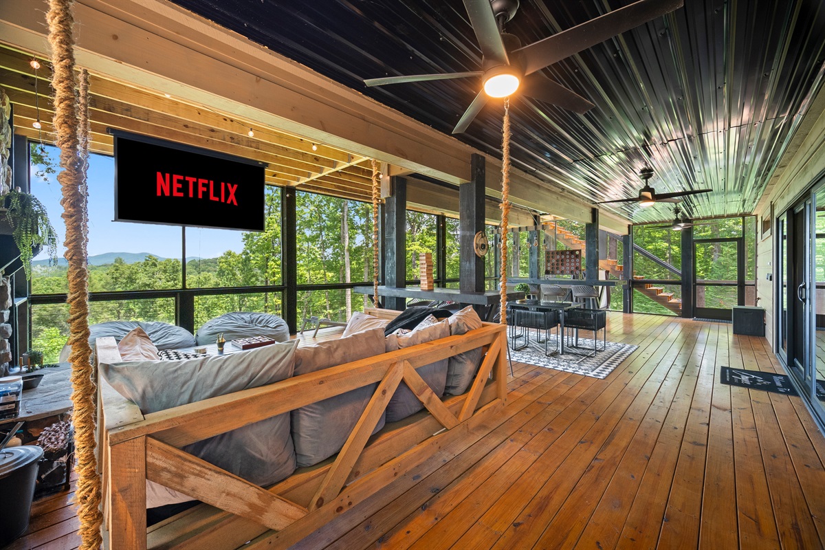 This spacious screened-in porch combines modern comfort with rustic charm, queen-size sofa bed, movie projector, lush greenery, and mountain views.