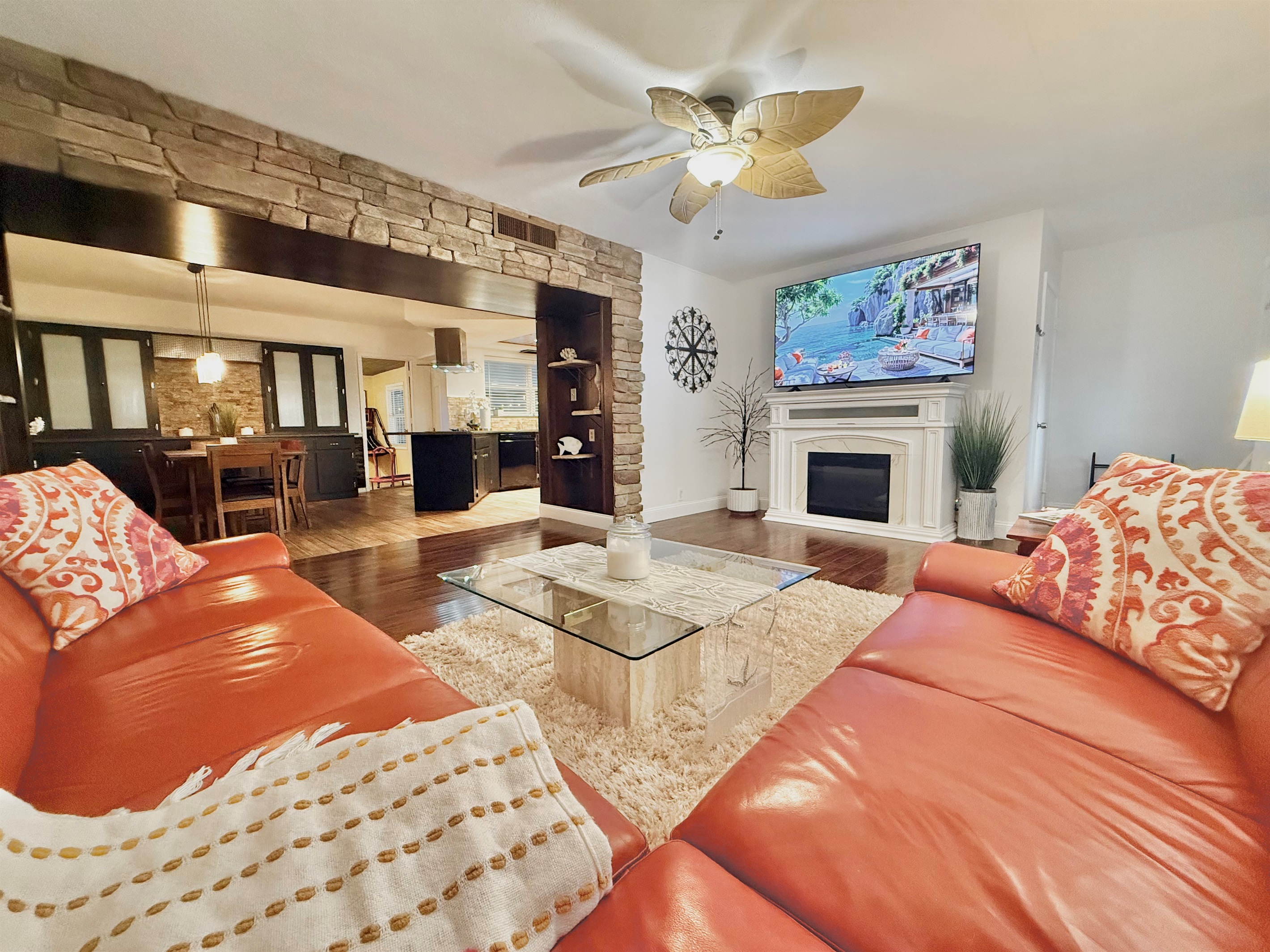 This inviting living room features a large wraparound sofa, warm wood floors, and a smart TV over a charming fireplace—perfect for movie nights or game-day lounging.