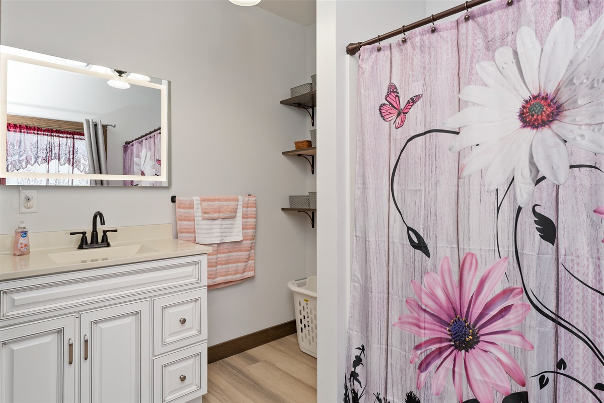 Freshly updated second floor bathroom with a floral shower curtain, elegant vanity, and practical shelving—designed for comfort and everyday convenience.