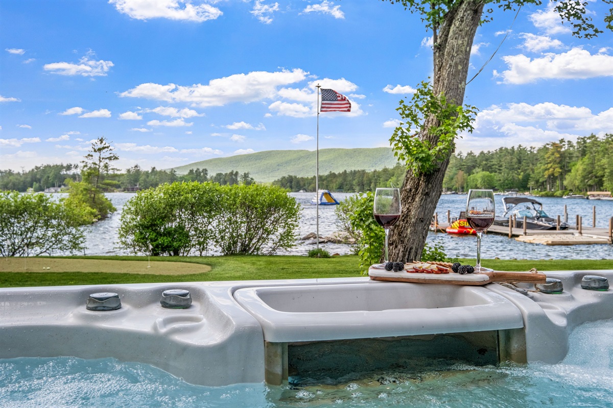 Hot tub with seating for 8 with its own tv, overlooking Lake Winnipesuakee and the mountain range in the distance
