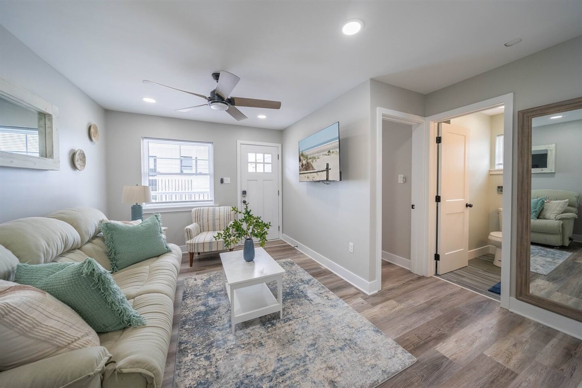 Comfortable living room with plush seating, ceiling fan, and bright natural light. Thoughtfully laid out with easy access to the bathroom and bedrooms, creating a calm, welcoming space to relax, watch TV, or unwind between outings.