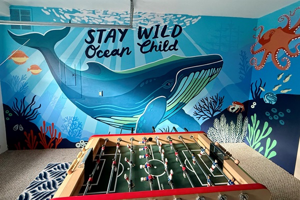 Game on with a splash of fun! 🐳 This garage game room brings the vibes, featuring a friendly whale mural and all the entertainment essentials- foos ball, pac man and The Simpson arcade games, giant connect four