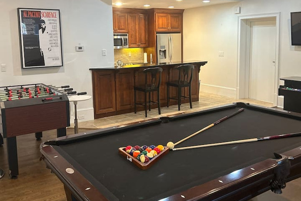 Game room with full kitchenette featuring custom cabinetry, granite bar, stainless steel refrigerator and microwave, recessed lighting, designer finished ceiling, pool table, foosball table, hardwood floors, and open layout ideal for entertaining.