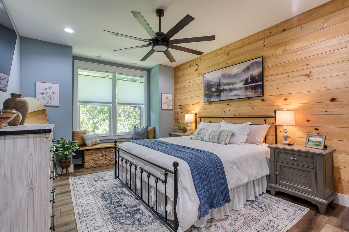 Retreat to the main-level king bedroom at Robbin’s Nest on Snowbird Creek, featuring a warm wood accent wall, bedside lamps, and a ceiling fan.