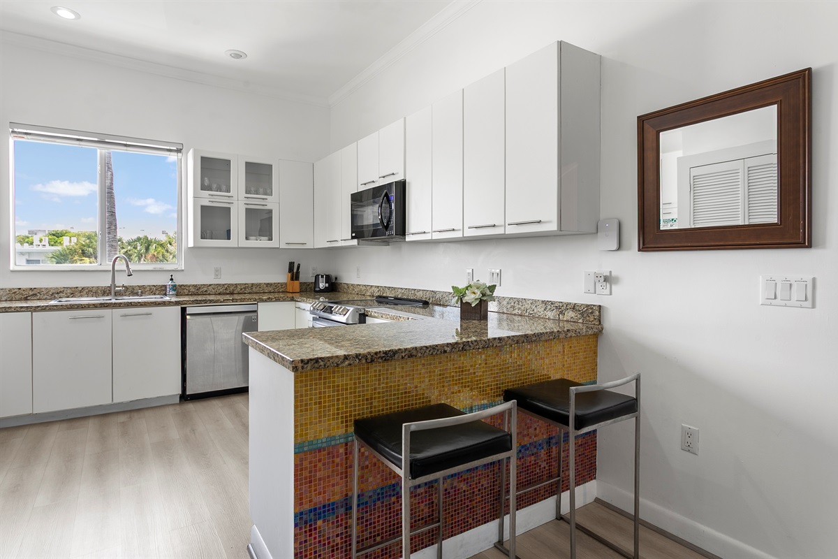 Mosaic tiled kitchen with modern appliances and breakfast counter. LG laundry tower behind closet doors