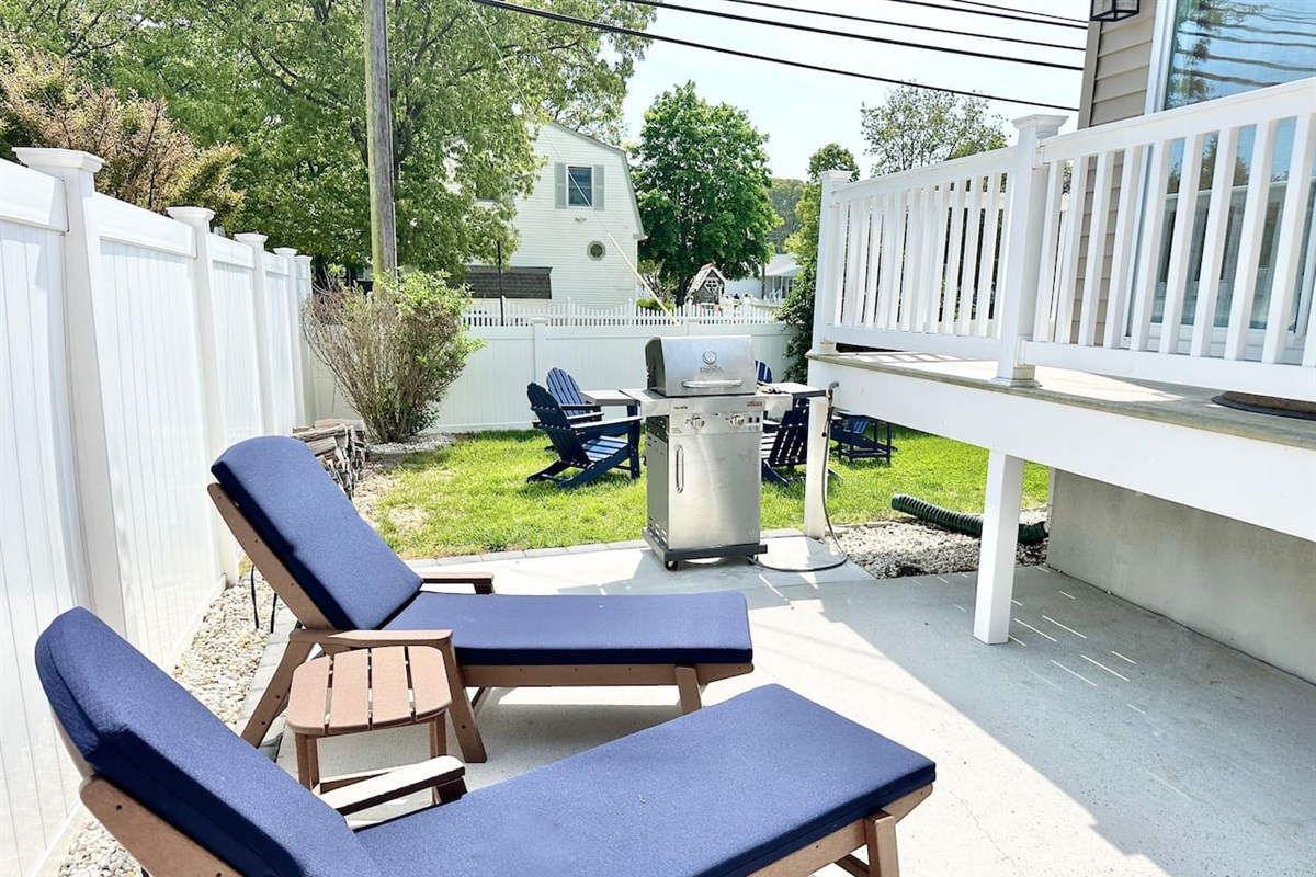 Enjoy the perfect outdoor setup for relaxation and dining. This fenced-in backyard features comfortable lounge chairs for soaking up the sun, a stainless steel grill for afternoon cookouts, and a grassy area with additional seating for the whole group.