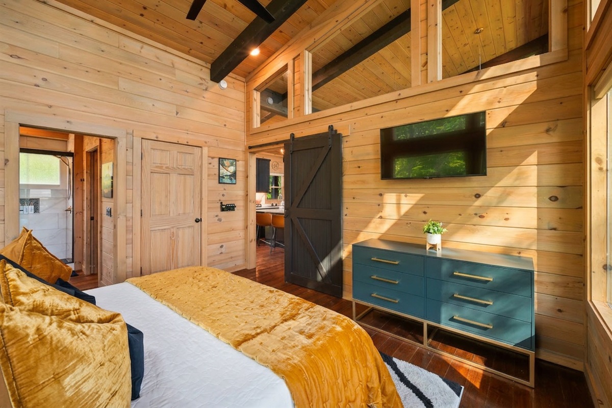 Sunlit rustic bedroom with warm wood walls, bold gold bedding, and a sleek barn door leading to the rest of the cabin
