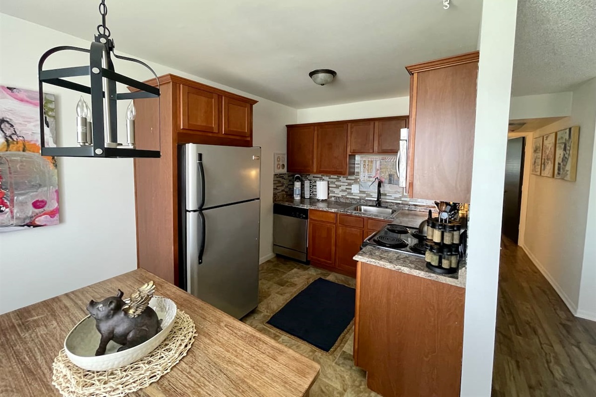 Stylish kitchen featuring stainless steel appliances, granite-look countertops, and warm wood cabinetry. The space opens to a cozy dining nook with unique decor, perfect for enjoying meals or morning coffee in comfort.