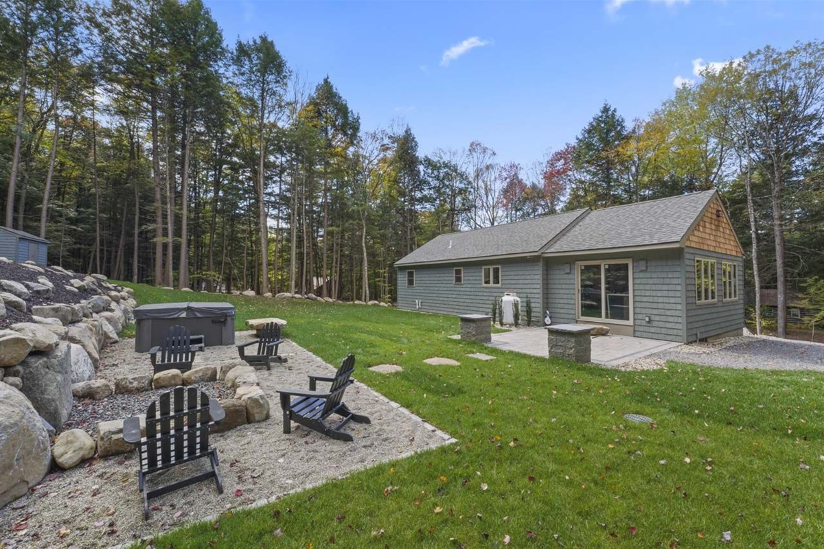 Back of house showing patio with couchman lights, firepit, hot tube and bolder wall