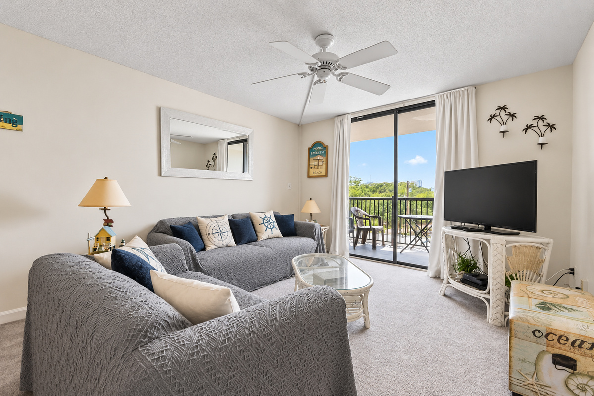 Living room with soft seating, TV, and balcony access at Holiday Towers, close to Myrtle Beach attractions.