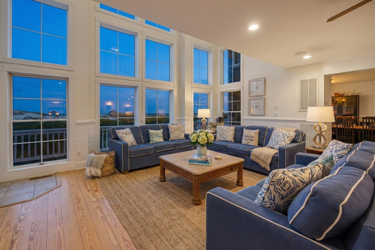 Soaring cathedral ceilings and a wall of floor-to-ceiling windows flood the living area with natural light and offer panoramic ocean views. Ample seating ensures the whole group can gather com
