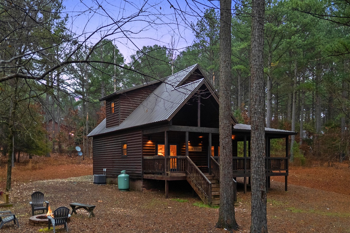 An exterior view highlights the cabin’s rustic charm and how naturally it blends into the wooded surroundings.
