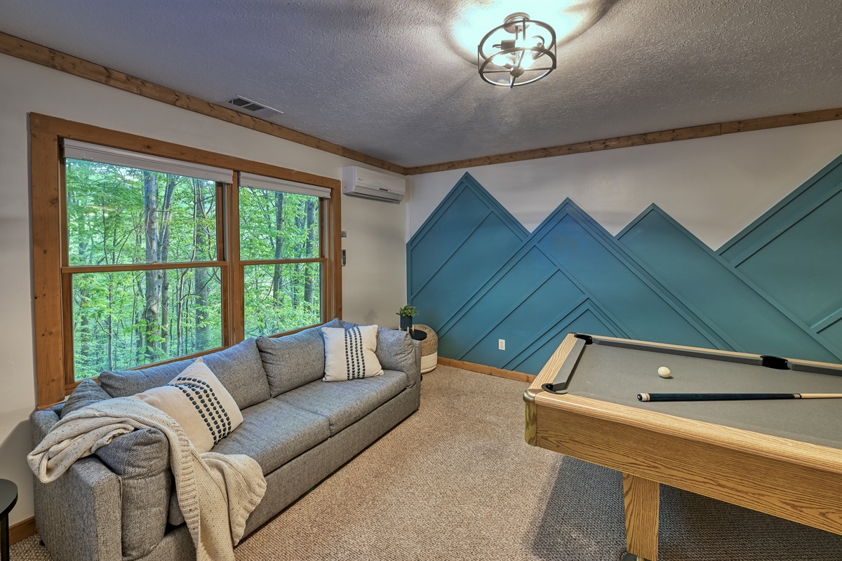 Lower level game room with pool table.  Looks out into the trees. 