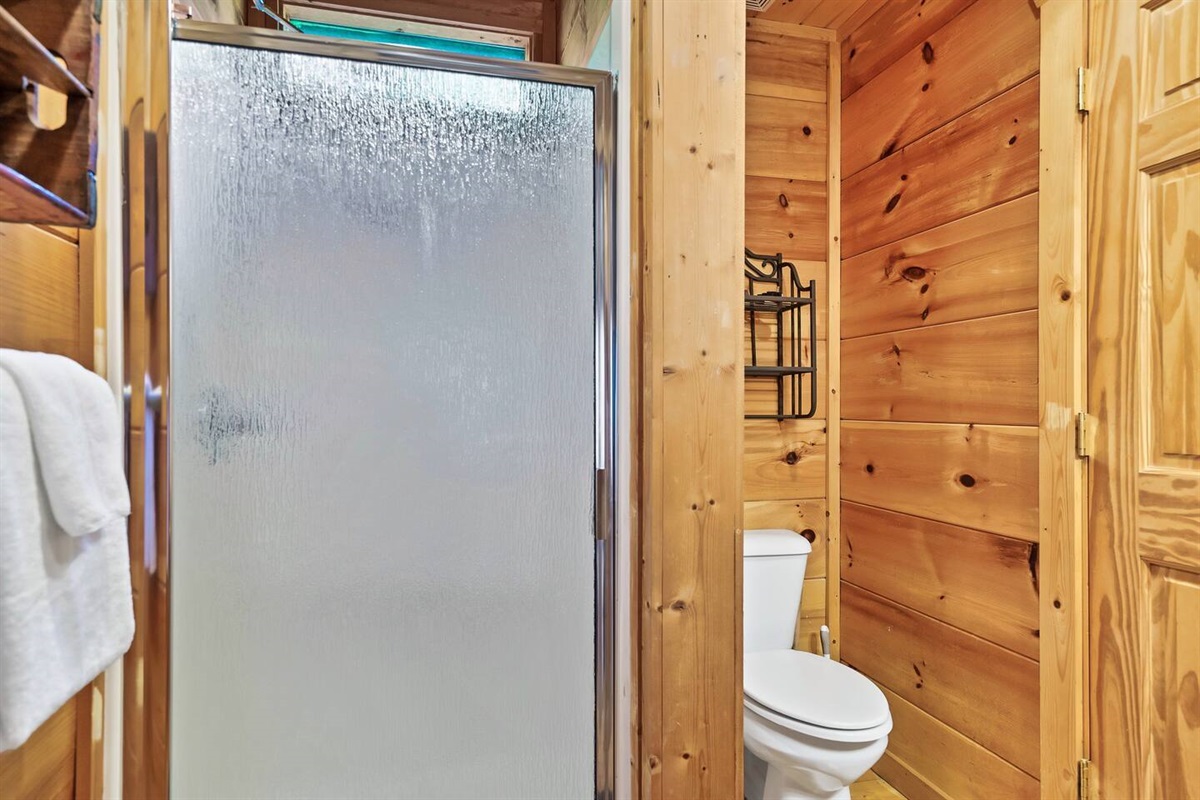 This compact bathroom combines a sleek frosted glass shower with natural wood tones, offering a functional and inviting space with an elegant yet rustic vibe.