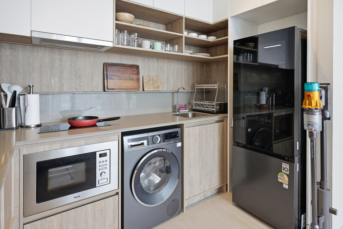 Kitchen with light wood cabinetry, stainless appliances, washing machine, and open shelving.