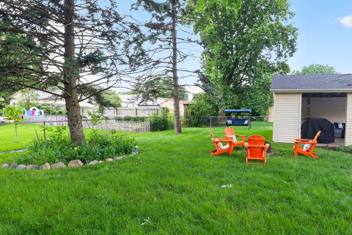 Flat, grassy backyard with a fire pit, glider swing, and room to relax or play.
