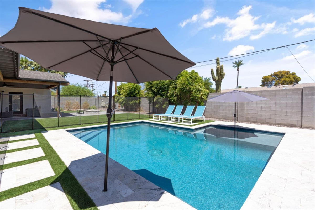 Private backyard pool with safety fence, lounge chairs, umbrella shade, fire pit seating, and a bright outdoor space 