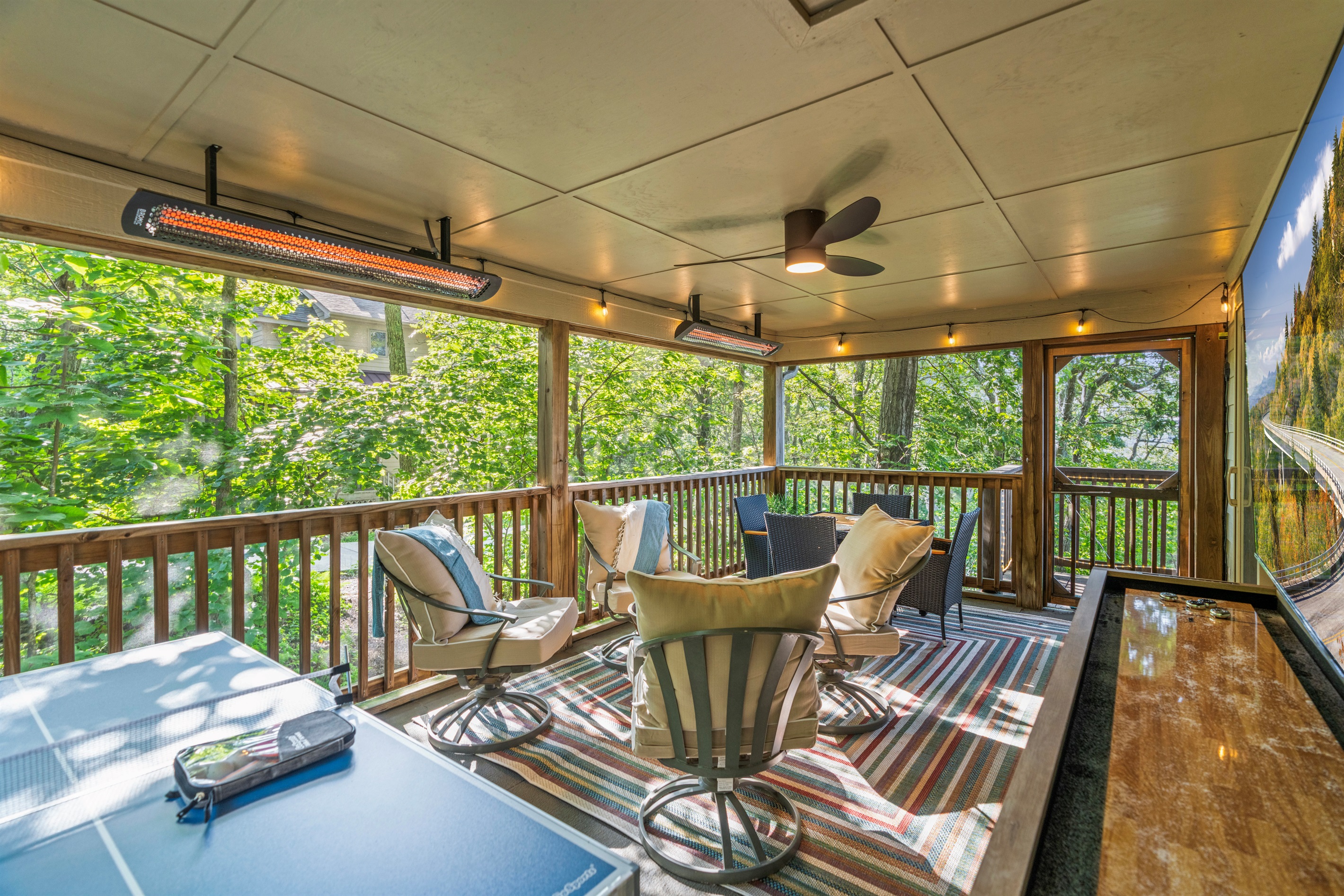 Treehouse vibes meet upscale amenities — shuffleboard, ping pong, 75" TV, and radiant warmth make this screened porch a year-round haven