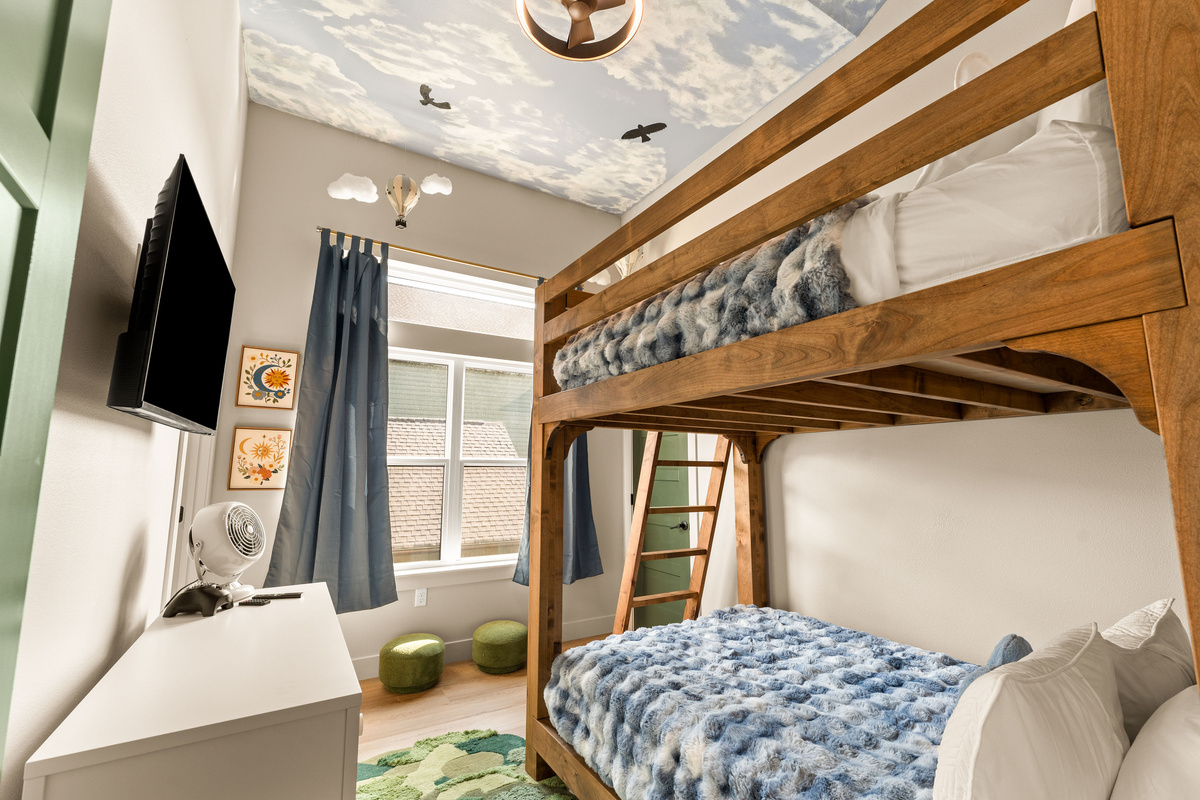  A bedroom made for little adventurers! Oversized wooden bunks, cozy blue bedding, a TV, and a dreamy sky ceiling complete with clouds, birds, and a hot-air balloon make bedtime part of the fun.