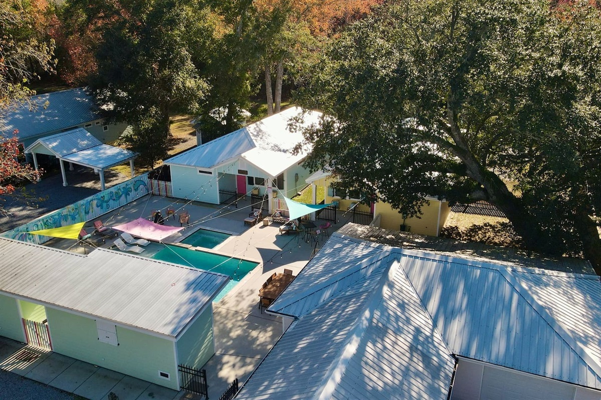 Aerial view of a vibrant retreat featuring colorful cottages, a central pool, and shaded outdoor gathering spaces.