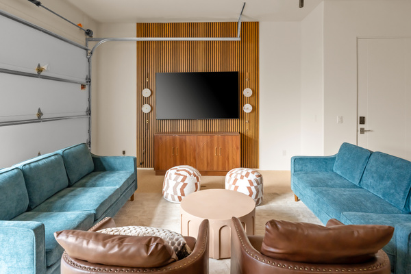 Movie night ready: deep teal sofas, leather armchairs, cozy poufs, and a large flat-screen 75" TV framed by modern timber paneling.